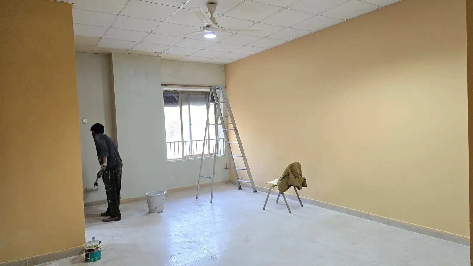 A large room being repainted, with a ladder and paint tools.
